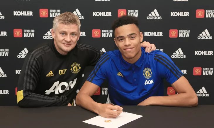 футболист подписывает контракт на фоне символики клуба